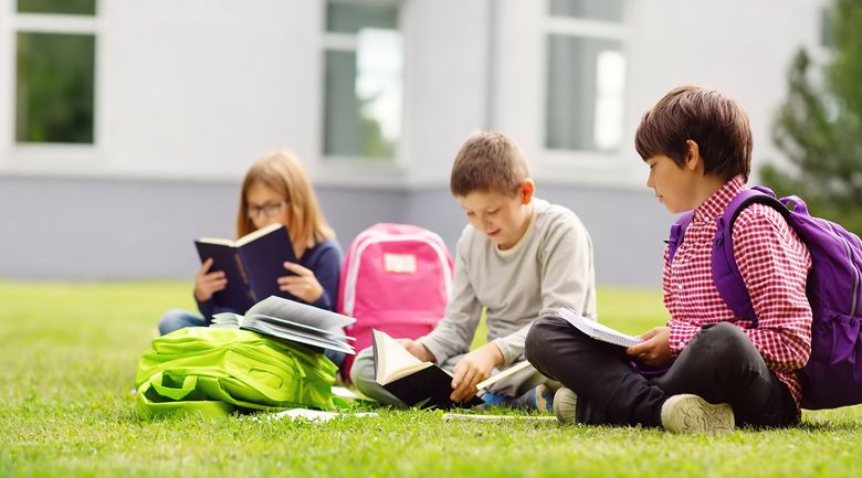 Schulkinder sitzen lesend auf der Schulwiese.