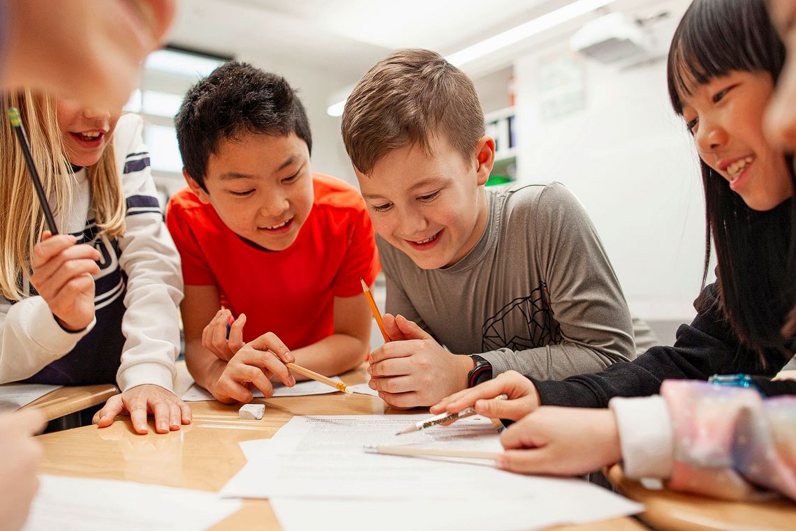 Einige lachende Kinder sitzen an einem Tisch und schauen gemeinsam auf ein Blatt Papier.