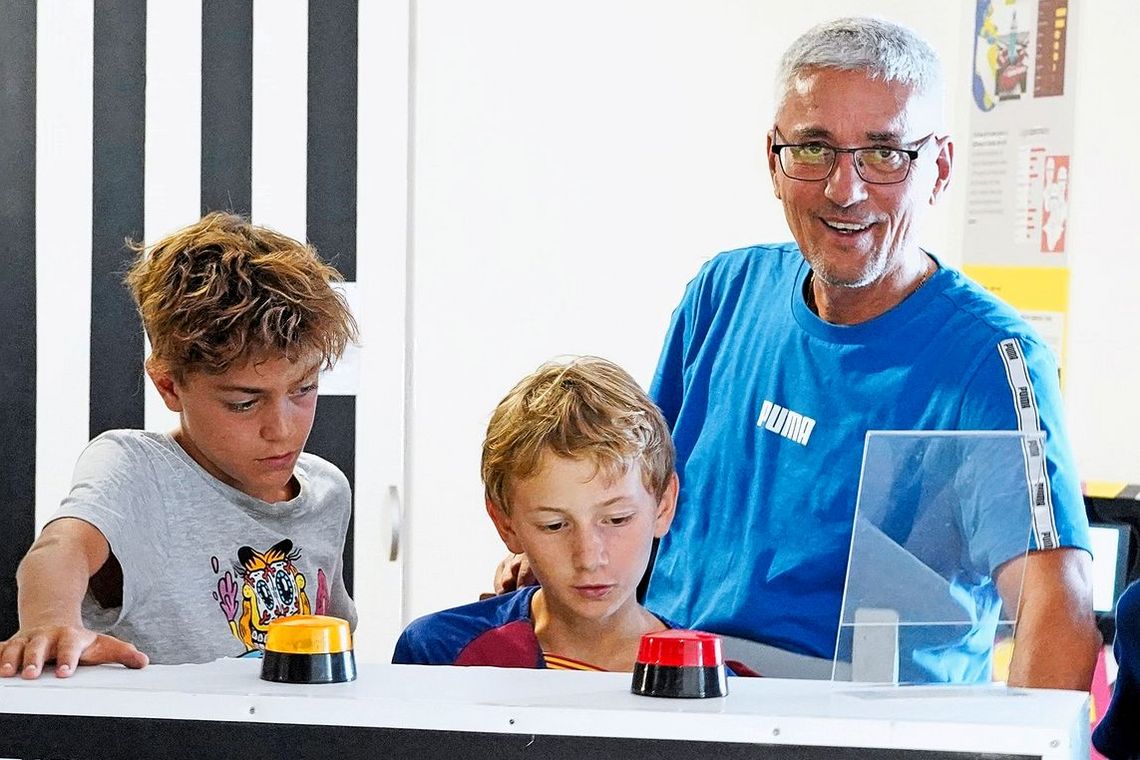 Ein Erwachsener Mann und zwei Kinder stehen vor einer Maschine, auf der sich zwei Warnlichter befinden.