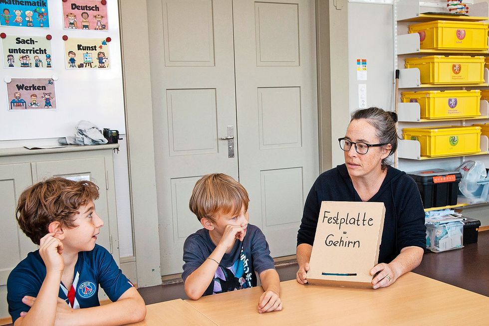 Primarschullehrerin Sara Cortellini zeigt einer Gruppe von Kindern einen Karton mit der Aufschrift "Festplatte". In diesem Karton befinden sich Karten mit Begriffen aus der digitalen Welt, die im Unterricht erklärt werden. Fotos: Roger Wehrli