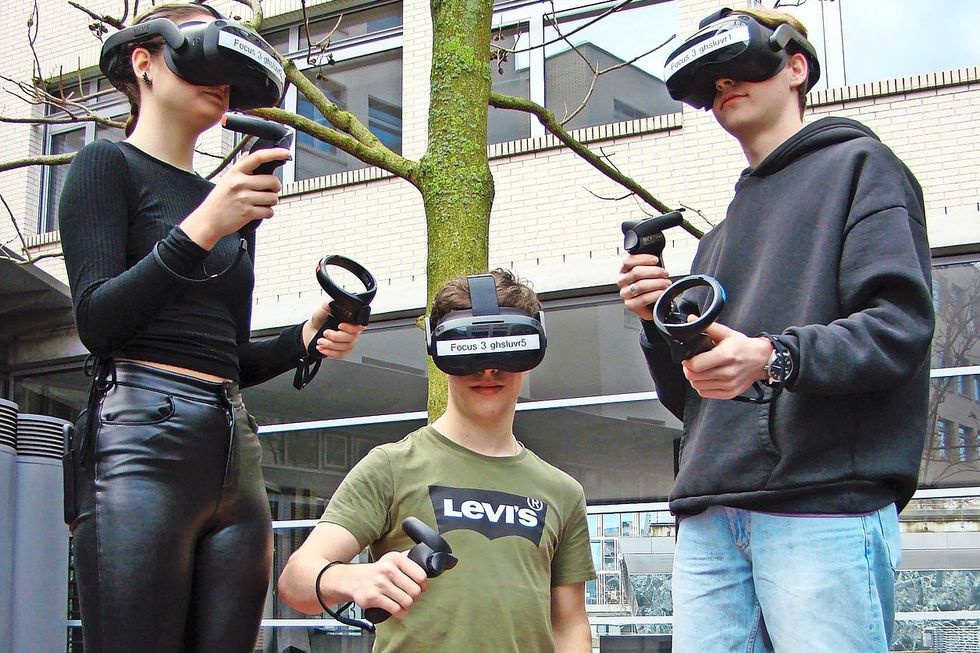 Drei Lernende tragen VR-Brillen und halten dabei Steuerelemente in ihren Händen.