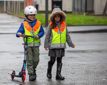 Zwei Schulkinder tragen eine orange-gelbe Leuchtweste.