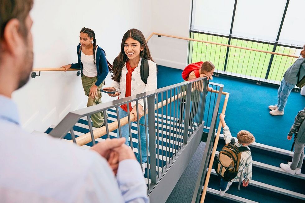 1820293481 Teacher Looking Down On Group Of Secondary Or High School Pupils Inside School Building On Stairs