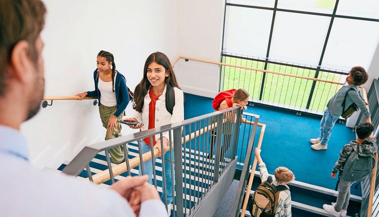 Teacher Looking Down On Group Of Secondary Or High School Pupils Inside School Building On Stairs