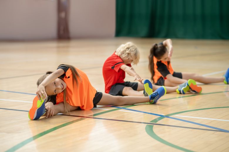Kinder dehnen in einer Turnhalle Beine und Arme