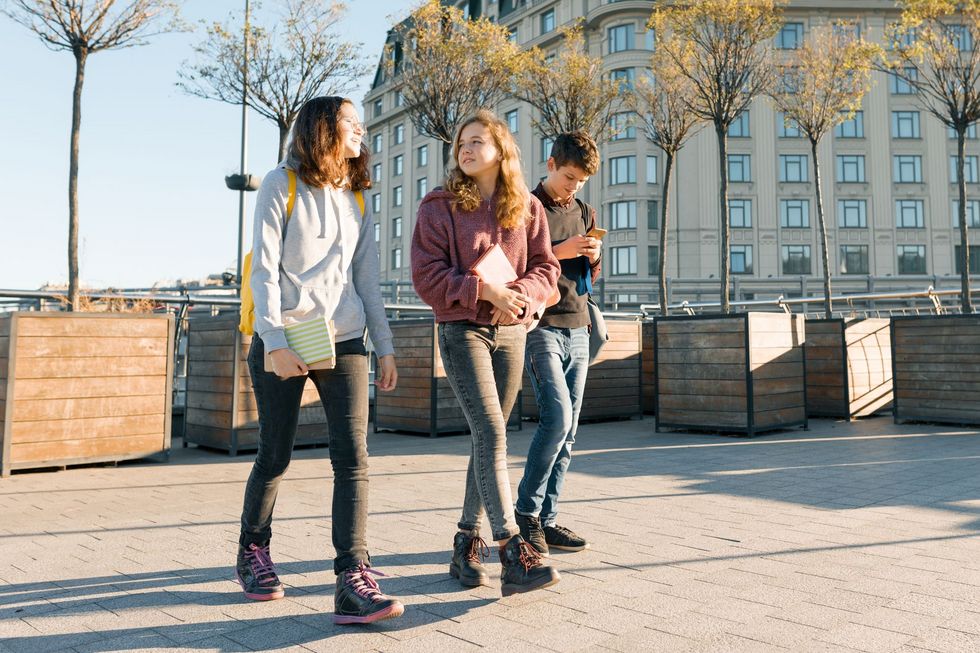 Outdoor portrait of teenage students with backpacks walking and talking. City background, golden hour Drei Jugendliche schlendern über einen Platz.