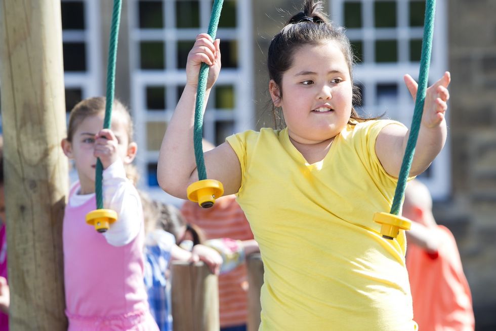 Auf dem Spielplatz turnt ein pummeliges Kind an Seilen.