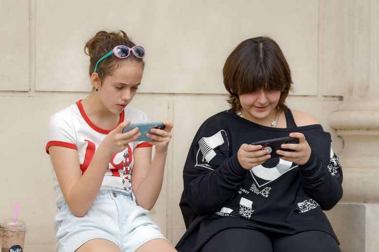 Zweimädchen sitzen auf einer Mauer und starren auf ihre Handys.