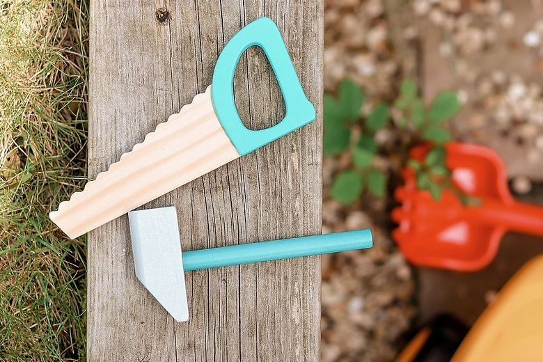 Eine Spielzeugsäge und ein Spielzeughammer liegen im Garten.