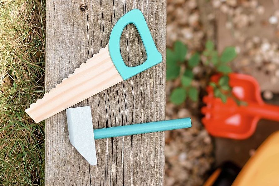 Eine Spielzeugsäge und ein Spielzeughammer liegen im Garten.