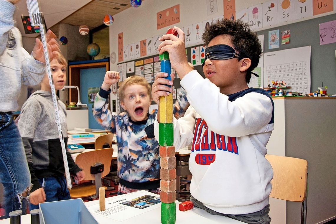 Ein Kind mit verbundenen Augen baut einen Turm aus Klötzen.