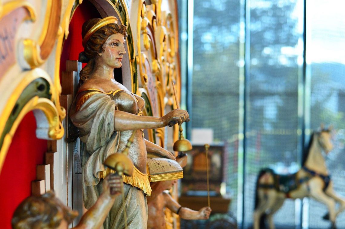 auf einer goldverzierten Orgel thront eine Frauenfigur, die eine Glocke in der Hand hält.