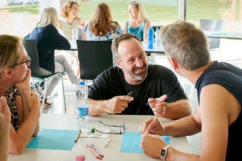 Drei Personen sitzen an einem Tisch und reden miteinander