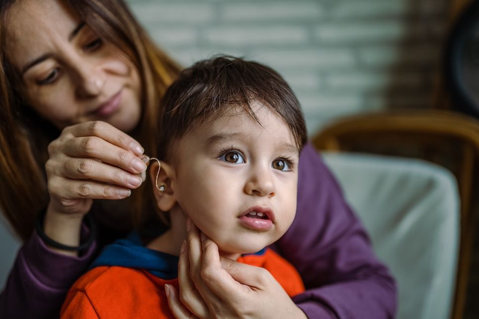 Mother helping her son with his Hearing Aid Kind mit einem Hörgerät.
