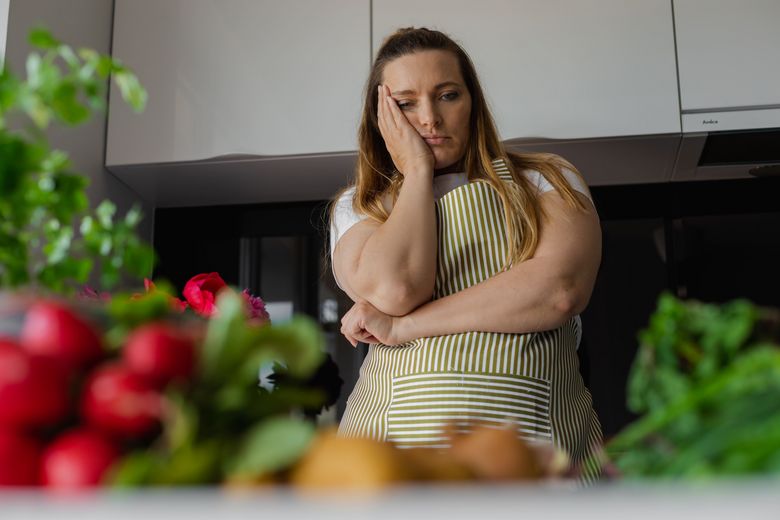 Eine Frau mit Küchenschürze blickt ratlos auf die verschiedenen Gemüse, die vor ihr auf der Küchenzeile liegen. Foto: iStock/Tatsiana Volkava