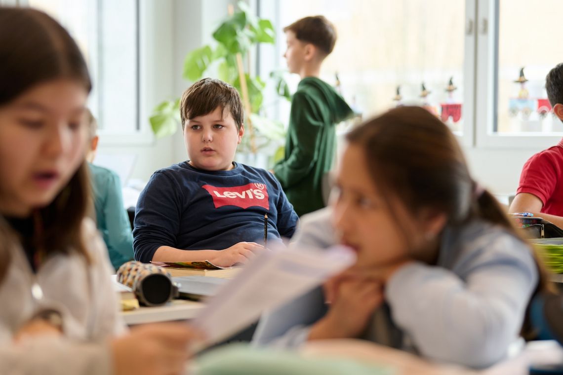 Erjan sitzt inmitten von Klassenkolleginnen und -kollegen im Schulzimmer.