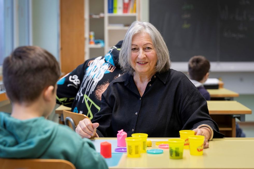 Frau mit grauen Haaren unterrichtet ein Kind.