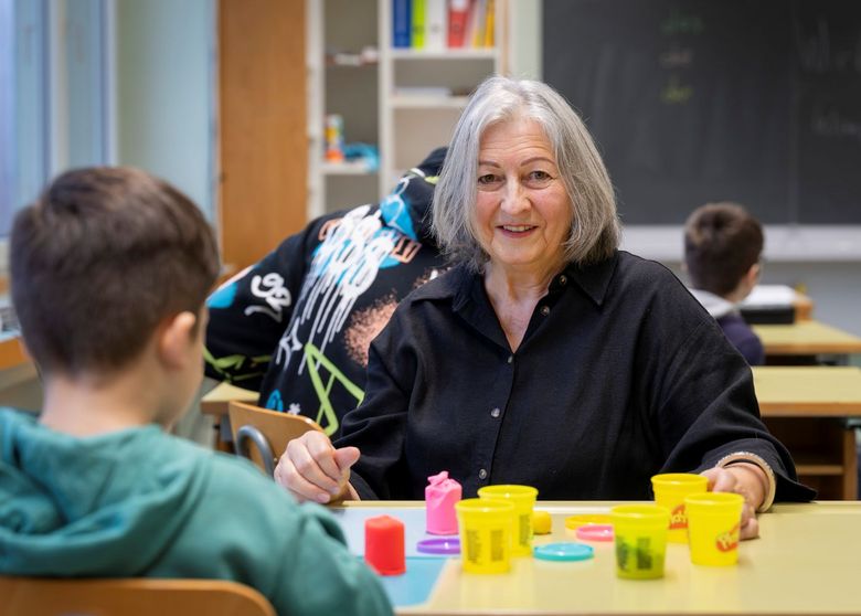 Frau mit grauen Haaren unterrichtet ein Kind.