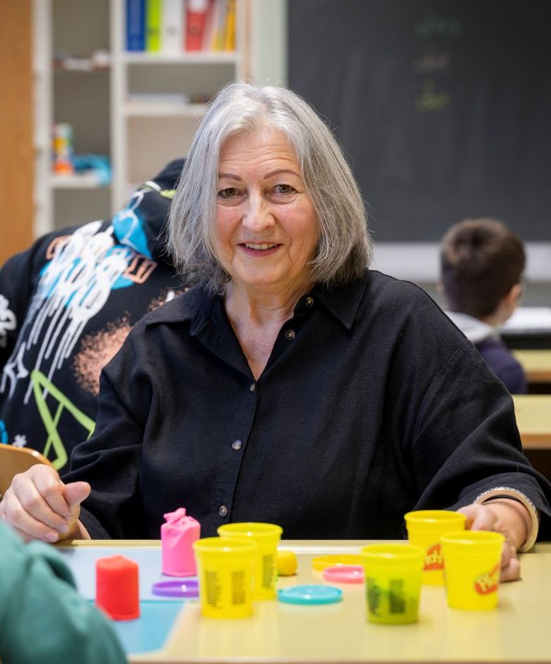Frau mit grauen Haaren unterrichtet ein Kind.