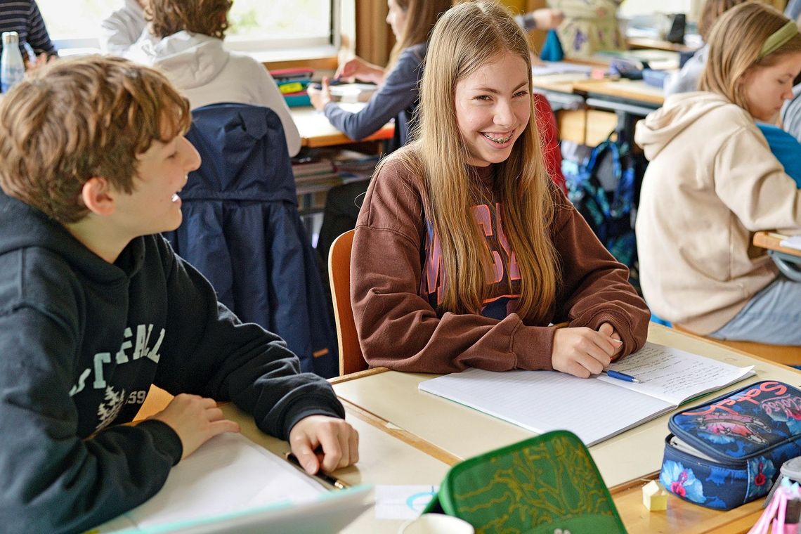 Schülerinnen und Schüler sitzen lachend vor ihren Heften.