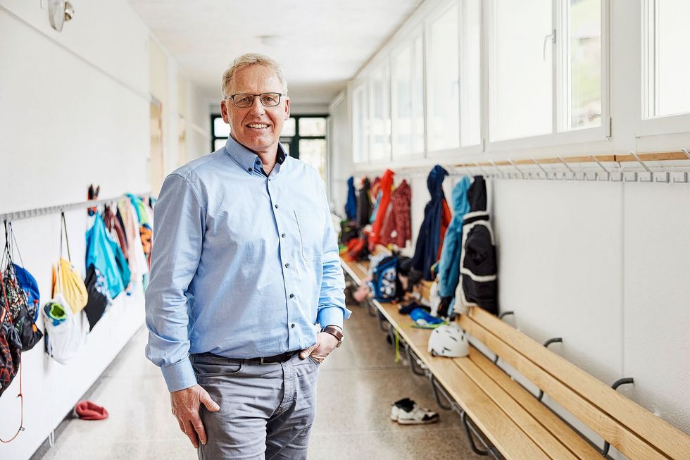 Michael Gerber steht in einem hellblauen Hemd im Gang eines Schulhauses.