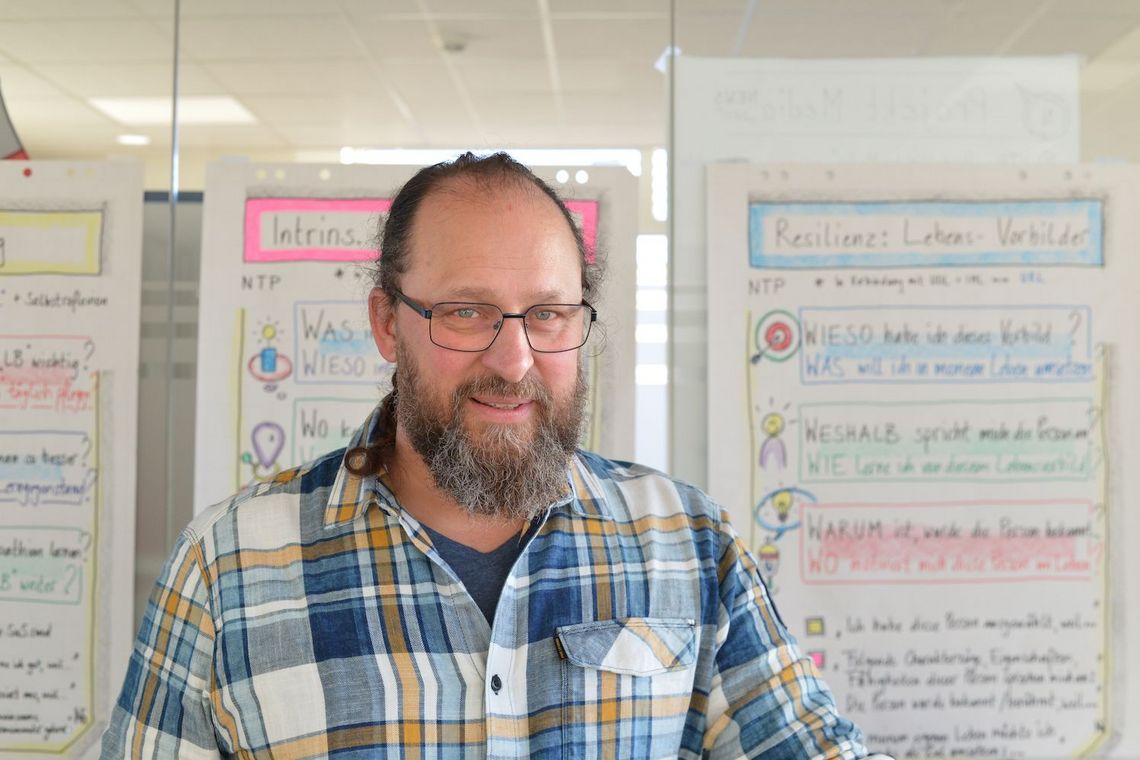 Stephan Herzer steht vor einer Wand mit Notiz-Postern.