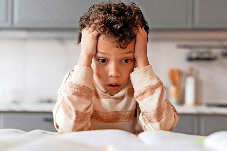 Ein Kind rauft sich die Haare und blickt auf einige offene Bücher, die vor ihm auf einem Tisch liegen.