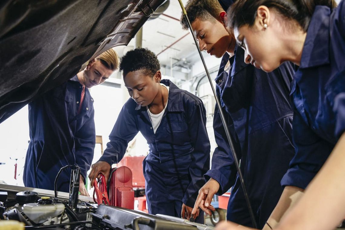 Jugendliche arbeiten gemeinsam an einem Automotor.