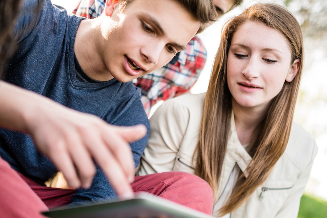 Eine Gruppe Jugendlicher schaut auf ein Tablet.