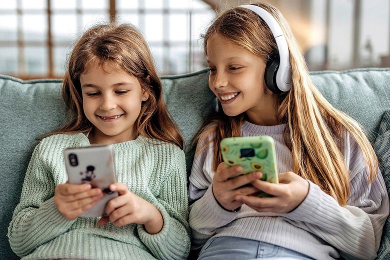 Zwei Mädchen auf einem Sofa lachen, während sie je ein Smartphone benutzen.