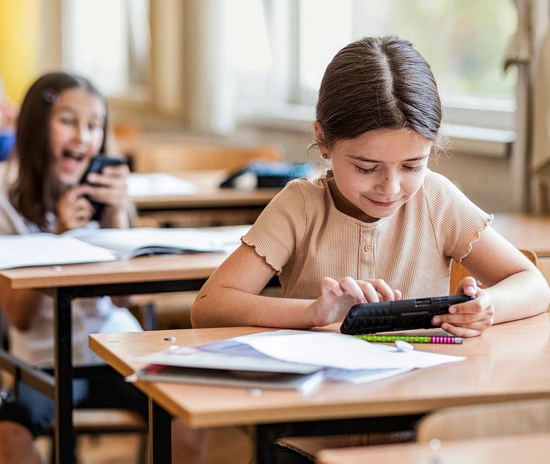 Kinder sitzen an Schulbänken und benutzen ihre Smartphones.