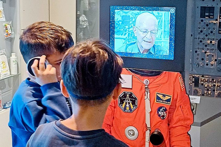 Knaben schauen einen Bildschirm an, auf dem ein Astronaut zu ihnen spricht