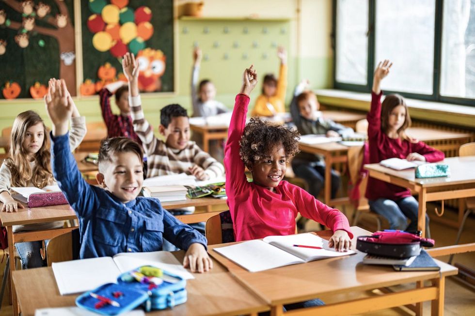 Schulkinder heben im Unterricht ihre Hand.