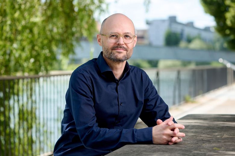 Porträtfoto von Christian Hugi, der mit dem Rücken zu einem Fluss steht.